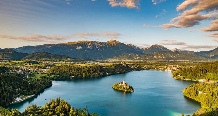 Otra vista amplia del brillante Lago Bled con la iglesia de la isla y los picos que lo rodean bajo cielos azules.