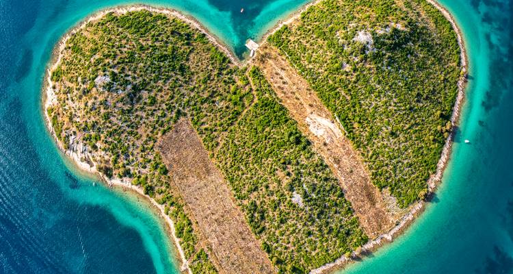 Aerial of heart-shaped lush green island surrounded by crystal-clear turquoise waters of the Adriatic.