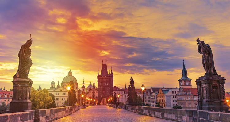 Dramatic sunrise over Charles Bridge with glowing sky and historic statues framing Prague’s skyline