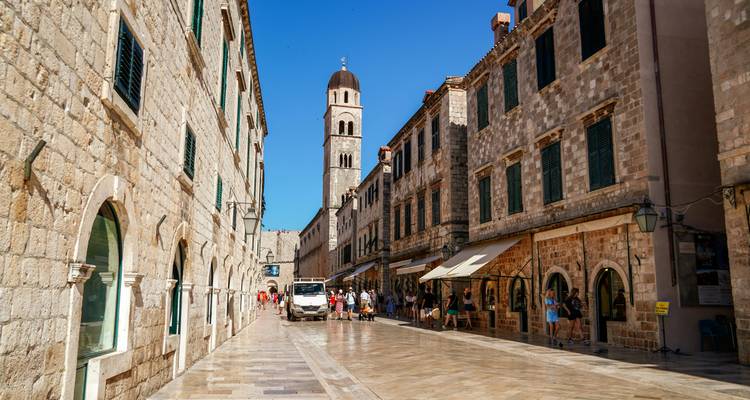 Sonnenbeschieneter Stradun, Dubrovniks polierte Kalkstein-Hauptstraße, gesäumt von historischen Steingebäuden und dem Franziskanerturm, belebt von Touristen.