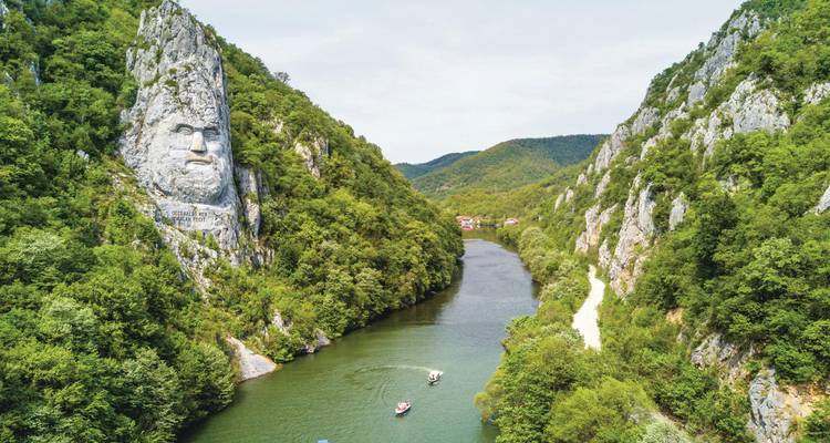 Garganta de río estrecha con una monumental escultura de piedra de la cara de Decebalo elevándose sobre los botes de turismo.