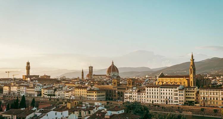 Vue panoramique de la ligne d'horizon de Florence au lever du soleil avec le Dôme, le Palazzo Vecchio et les toits de la ville baignés dans une lumière chaude.