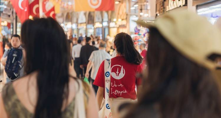 Pasillo concurrido del Gran Bazar de Estambul con compradores y banderas turcas colgando arriba, enfoque en un miembro del tour de Intrepid.