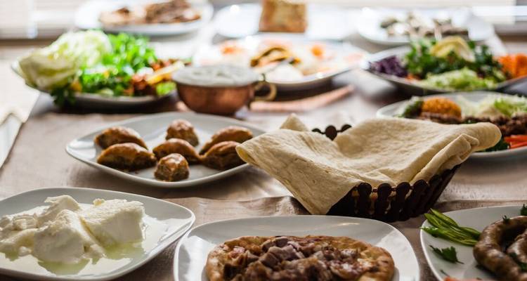 Una generosa variedad de platos turcos tradicionales incluyendo baklava, pan plano, ensaladas y yogur en una mesa iluminada por el sol.