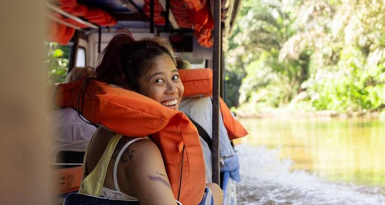 Smiling woman in life jacket rides an open boat along a jungle river in Costa Rica.
