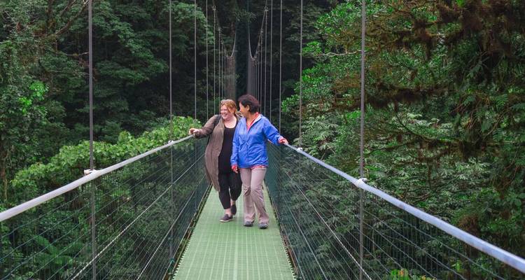 Two women cross a green hanging bridge above Monteverde’s cloud forest.