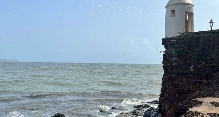 Bastion de pierre avec une petite tourelle blanche s'élevant au-dessus d'une mer grise agitée et de rochers noirs.