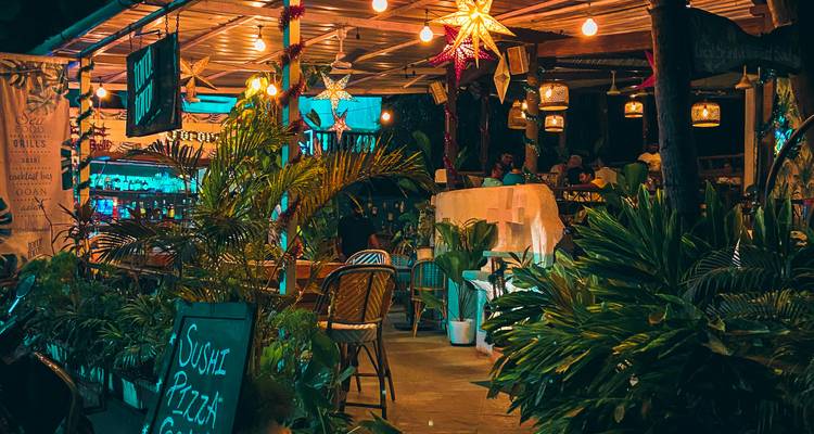 Restaurant-bar en plein air confortable, illuminé par des lanternes étoilées suspendues et entouré de plantes tropicales la nuit.