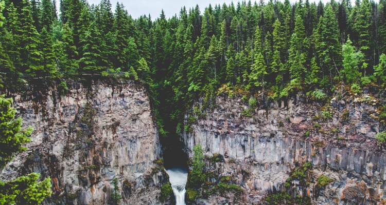 Tiefe bewaldete Schlucht mit Wasserfall, der zwischen rauen Felswänden in British Columbia hinabstürzt.