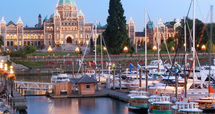 Abendlicher Blick auf Victorias beleuchtete Parliament Buildings und den Inner Harbour mit Yachten.