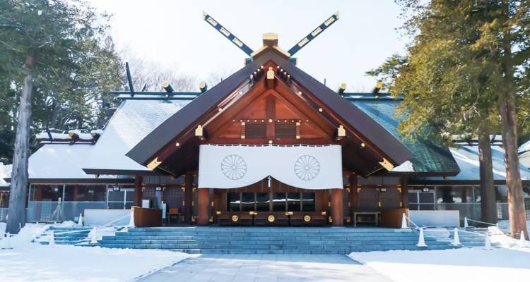 Schneebedeckter Shinto-Schrein mit klarer Holzarchitektur und weissen Vorhängen an einem hellen Wintertag.