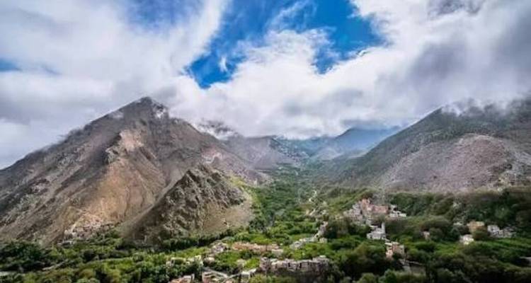 Vallée de montagne spectaculaire avec des villages dispersés sous des nuages dynamiques dans le Haut Atlas.
