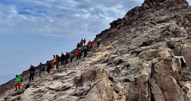 Ligne de randonneurs traversant une pente rocheuse accidentée en route vers le sommet du Mont Toubkal.