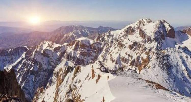 Les premiers rayons du soleil illuminant les sommets et vallées enneigés du Haut Atlas de leur lumière chaleureuse.