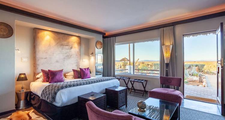 Habitación elegante de lodge con una cómoda cama king size, iluminación cálida y una gran ventana con vistas al paisaje semidesértico.