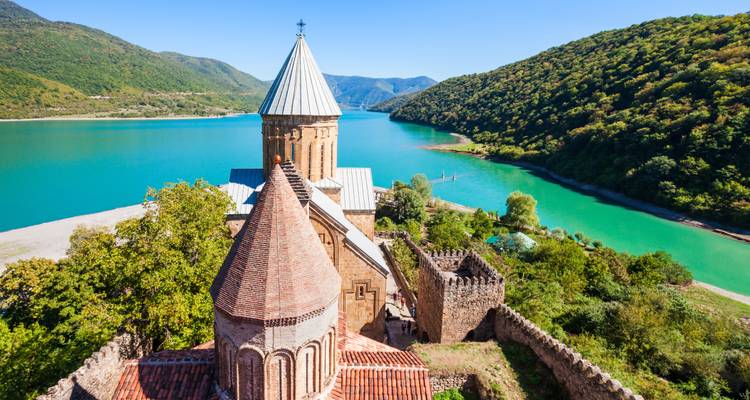 Die Ananuri-Festung und Kirche mit Blick auf das türkisfarbene Stausee Zhinvali inmitten bewaldeter Hügel.