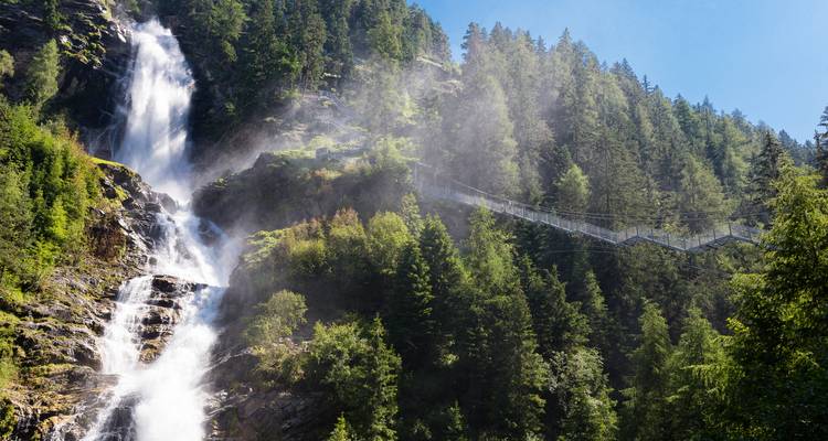 Dramatische alpentwaterval die door beboste kliffen naar beneden stort naast een hoge hangebrug