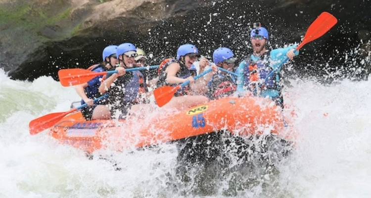 Wildwasser-Rafting-Enthusiasten in blauen Helmen, die mit einem orangefarbenen Floss durch Stromschnellen fahren