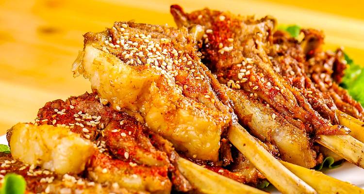 Primer plano de chuletas de cordero a la parrilla espolvoreadas con semillas de sésamo y especias sobre un plato de verduras.