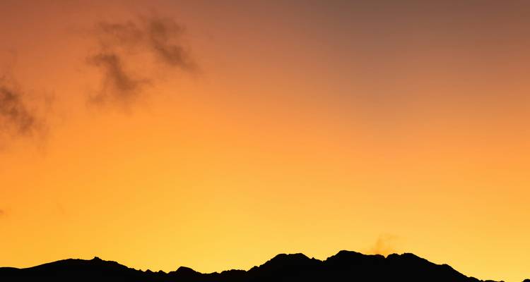 Silueta de una cordillera distante bajo un cielo de amanecer naranja vivido en Perú.