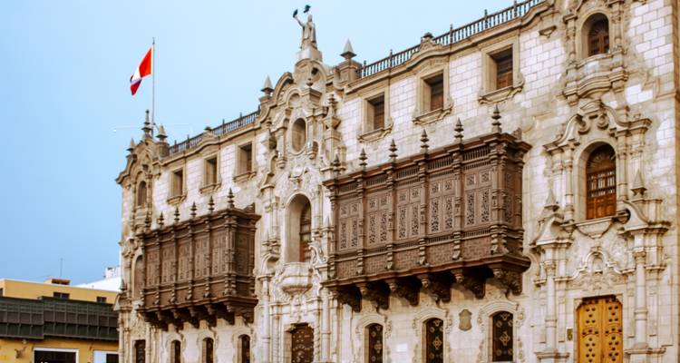 Fachada barroca del Palacio Arzobispal de Lima con balcones de madera elaborados y la bandera peruana ondeando.