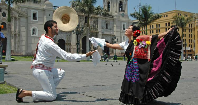 Los bailarines tradicionales peruanos realizan una rutina folclórica en una plaza con una iglesia colonial de fondo.