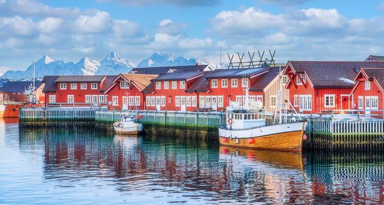 Les cabanes de pêcheurs rouge emblématique bordent un port tranquille avec des pics enneigés en arrière-plan aux îles Lofoten.