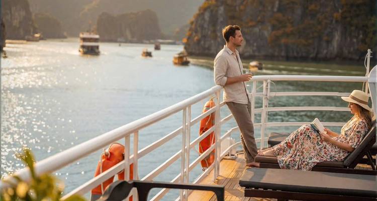 Un couple se détendant avec des boissons sur le pont d'une croisière dans la baie d'Halong au milieu des paysages karstiques.