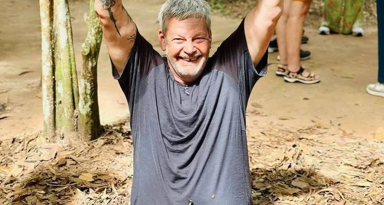 Homme émergeant souriant de l'entrée étroite du tunnel de Cu Chi entouré par le sol de la forêt.