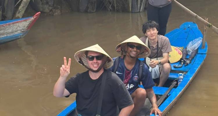 Les voyageurs portant des chapeaux coniques assis dans une barque en bois bleu sur les eaux boueuses du Mékong, faisant le signe de la paix.