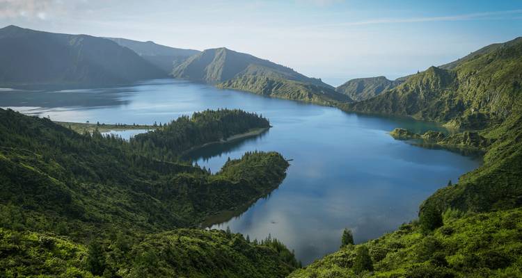 Spectacular volcanic lake surrounded by steep green mountains under clear blue sky.