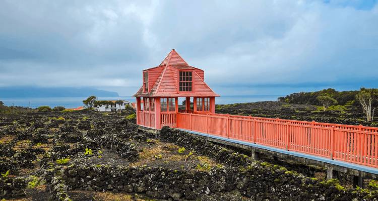 Small red wooden lookout pavilion and boardwalk crossing a rugged black lava field with ocean in the distance under cloudy skies.