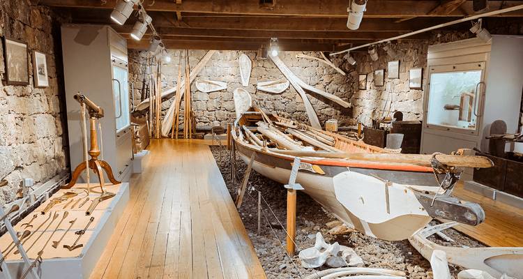 Historic whaling boat displayed inside a stone-walled maritime museum with wooden floors and nautical artifacts.