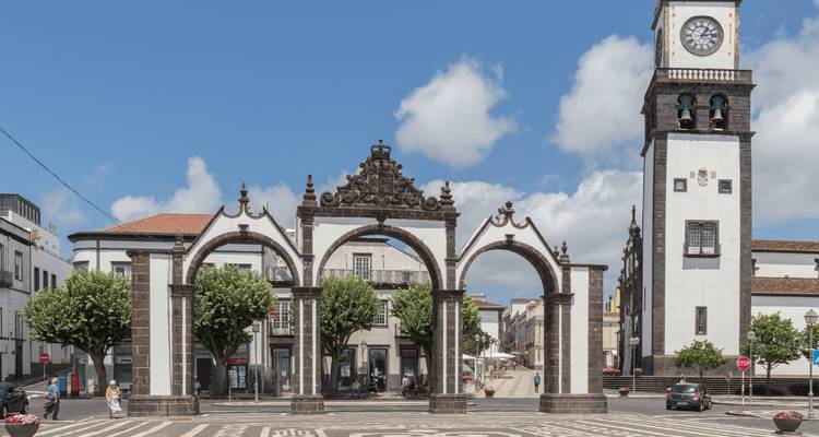 Iconic three-arched city gates and clock tower on a sunny plaza in a whitewashed Azorean town.