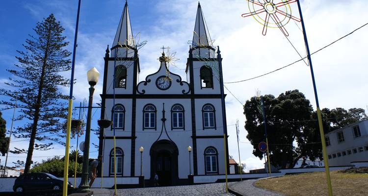 White twin-spired parish church with black trim and decorative lights set against a blue sky.
