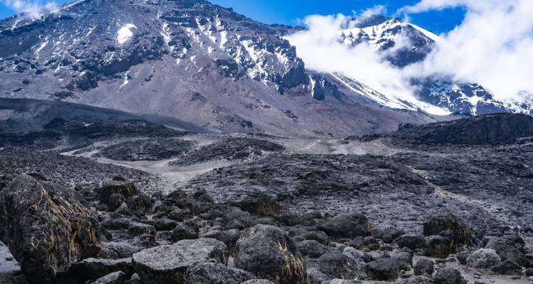 Kale rotsachtige hellingen met plekjes verse sneeuw en drijvende wolken op Kilimandjaro's bovenste berggedeelte.