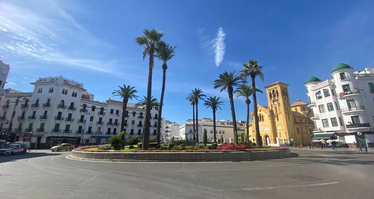Brede rotonde in Tetouan omzoomd met palmen, historische wit en gele gebouwen onder een heldere hemel.
