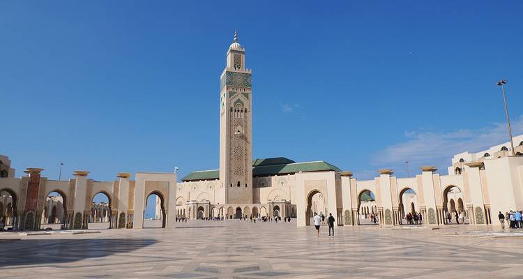 Uitgestrekte binnenplaats van de Hassan II-moskee met torenhoge minaret tegen een levendige blauwe lucht.