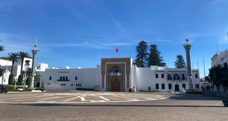 Witgekalkt koninklijk paleizencomplex met een centraal poort en Marokkaanse vlag op een open plein.