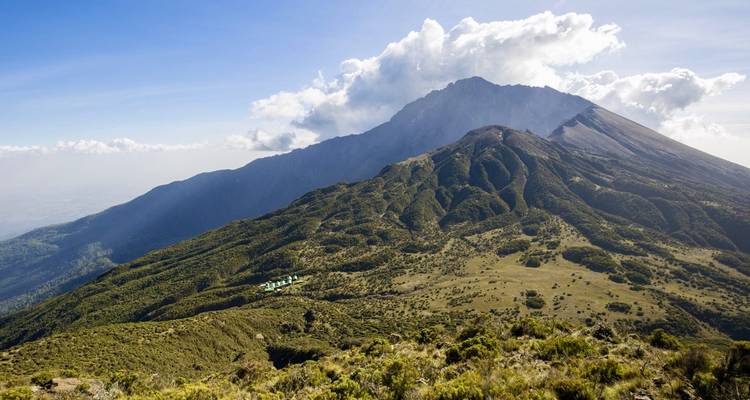 Breed uitzicht op de beboste hellingen en alpine weiden van de Mount Meru met kleine hutjes met groene daken die op de bergkam zijn genesteld.