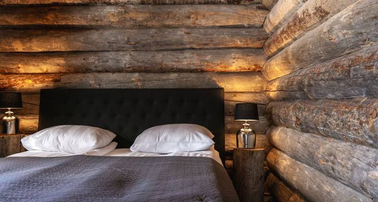 Chambre de cabane en rondins chaleureusement éclairée dotée d'une tête de lit rembourrée foncée entre des murs en bois rustiques.