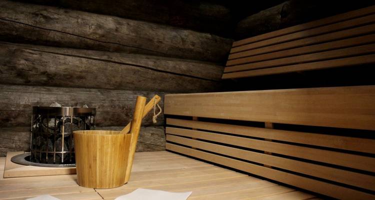 Intérieur traditionnel de sauna en bois avec sièges en banc, poêle en pierre et seau à eau en bois.