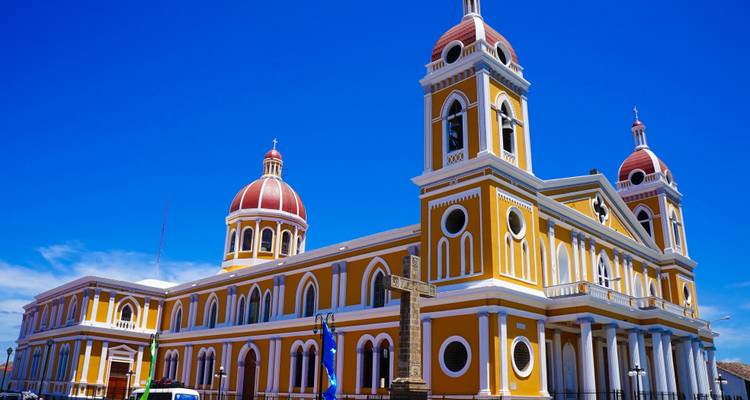 Die leuchtend gelbe und weiße Kathedrale von Granada steht vor einem tiefblauen Himmel mit roten Kuppeltürmen.