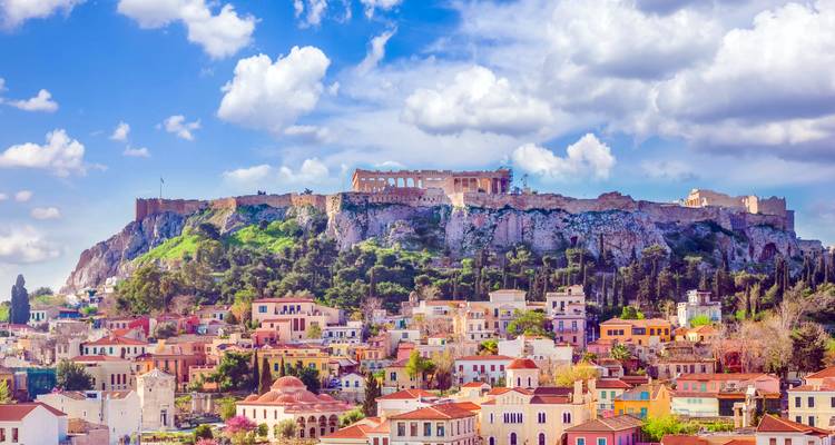 Vista diurna de la Acrópolis elevándose sobre los techos coloridos de Atenas bajo nubes esponjosas