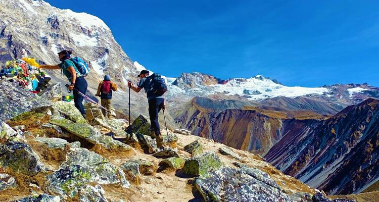 Les alpinistes montent un sentier alpin rocheux avec les pics enneigés de Langtang se dressant majestueusement à l'arrière-plan.