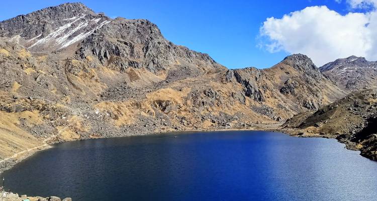 Lac alpin d'un bleu profond niché par des montagnes rocheuses stériles sous un ciel lumineux.