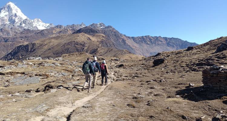 Un petit groupe de trekkers suit un sentier rocailleux à travers les hauts plateaux arides en direction des pics enneigés.