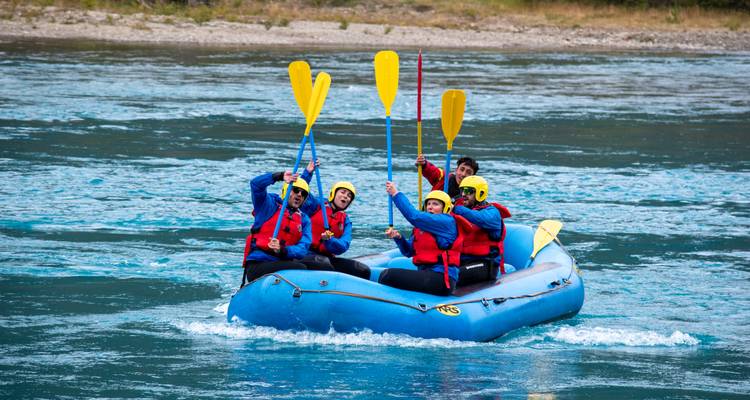 Group of rafters in blue raft raise paddles triumphantly on turquoise river.