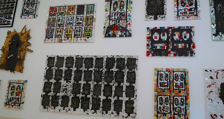 Verschiedene farbenfrohe moderne Kunstwerke an einer weißen Galeriewand angebracht.