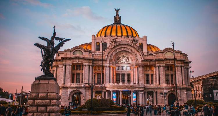Ikonische Sonnenuntergangsansicht des Palacio de Bellas Artes mit Fußgängern im Vordergrund und rosigem Himmel oben.